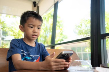 Küçük anaokulu çocuğu kafeteryada oturan akıllı telefonu kullanıyor.