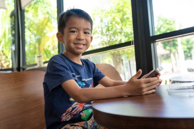 Küçük anaokulu çocuğu kafeteryada oturan akıllı telefonu kullanıyor.