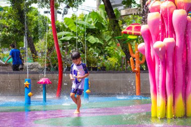 Küçük Asyalı anaokulu çocuğu yaz etkinliklerindeki açık su parkında eğleniyor.