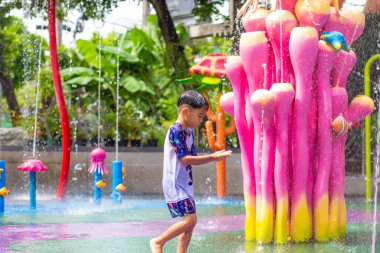 Küçük Asyalı anaokulu çocuğu yaz etkinliklerindeki açık su parkında eğleniyor.