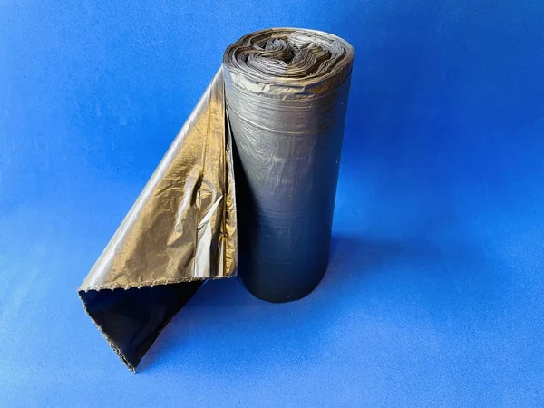 蓝色背景上的一卷垃圾袋垃圾袋 灰色表面上黑色箔的蓝色卷曲 顶部视图 — 图库照片