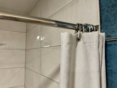 Perde duşta. Duş al. Duşta döşeme. Banyo perdesi kancaları. Gri arka planda beyaz havluyla bir banyonun dikey görüntüsü.