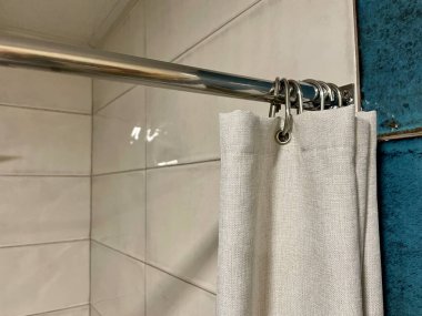 Perde duşta. Duş al. Duşta döşeme. Banyo perdesi kancaları. Gri arka planda beyaz havluyla bir banyonun dikey görüntüsü.