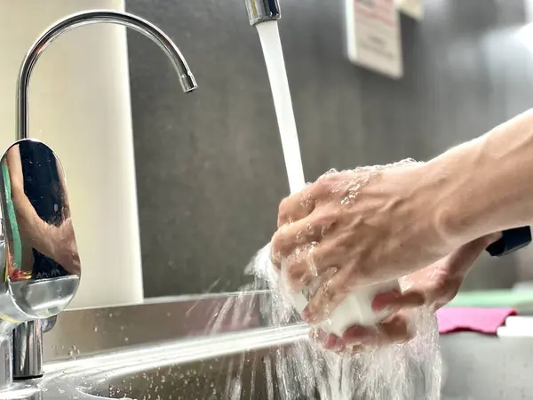 女は食器を水で洗う 手で水でシンクを掃除します 男の手を閉じて石鹸を洗う — ストック写真