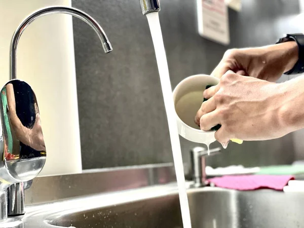 女は食器を水で洗う 手で水でシンクを掃除します 男の手を閉じて石鹸を洗う — ストック写真
