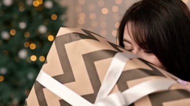 Gülümseyen ve yüzünü hediye kutusunun arkasına saklayan güzel genç bir kadının yakın çekimi..