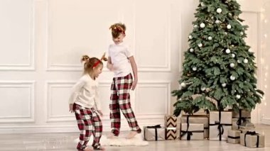 Two Cheerful Children are Running Around the Living Room in Their Pajamas Near the Christmas Tree.