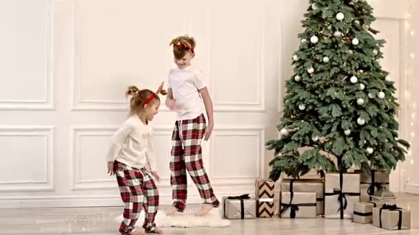 2人の陽気な子供がクリスマスツリーの近くの彼らのパジャマでリビングの周りを走っています — ストック動画