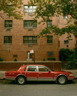 New York, Rego Park 'ta, yapraklı ağaçların altında, tuğladan bir apartmanın önüne park edilmiş klasik kırmızı bir Town Car var..