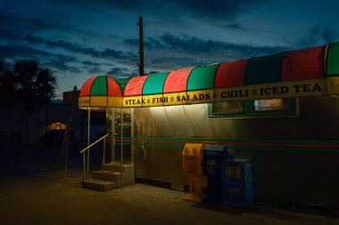 Angels Dining Car with its brightly lit, colorful awning advertising steak, fish, salads, chili, and iced tea against a darkening sky in Palatka, Florida. clipart