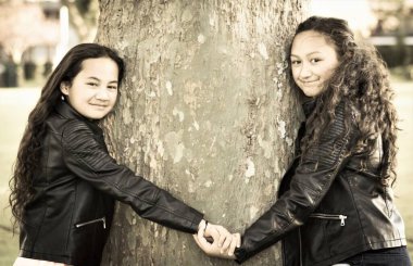 İki Maori kız kardeş gün içinde dışarıda bir ağaca sarılıyorlar.