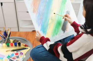 Sanat konsepti, Asyalı kadın ressam sandalyede oturuyor ve resim yapmak için tuval tutuyor..