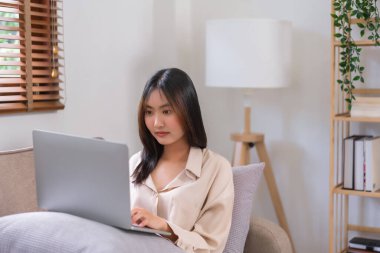 Oturma odasında faaliyet kavramı, sosyal medyada sörf yapmak için dizüstü bilgisayara veri yazan genç Asyalı kadın..