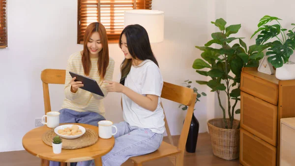 Relax at home concept, LGBT lesbian couple pointing and looking on tablet while working together.