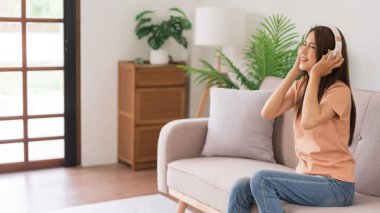 Evde faaliyet kavramı, kulaklıklı genç bir kadın kanepede otururken müzik dinler ve şarkı söyler..