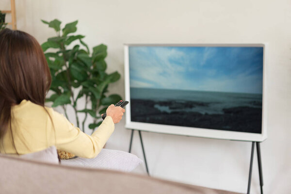 Leisure activity concept, Young woman holding remote control to changing channel and eating popcorn.