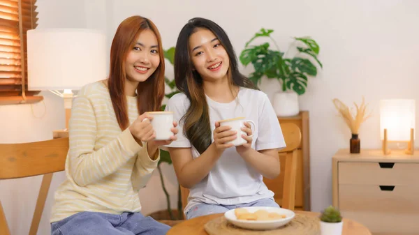 Relax at home concept, LGBT lesbian couple holding coffee cup and smiling to looking at camera.