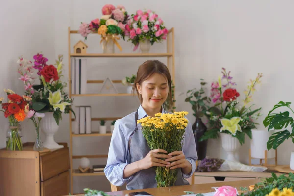 Florist concept, Woman florist smells yellow chrysanthemum while making bouquet in flower shop.
