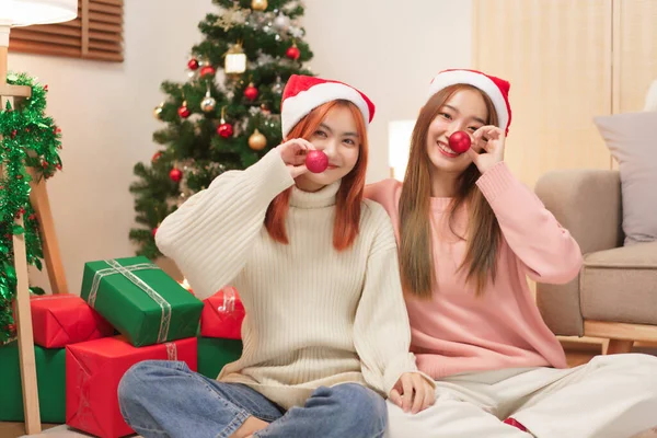 Christmas celebration concept, Two women in santa hat and covering nose with red christmas ball.
