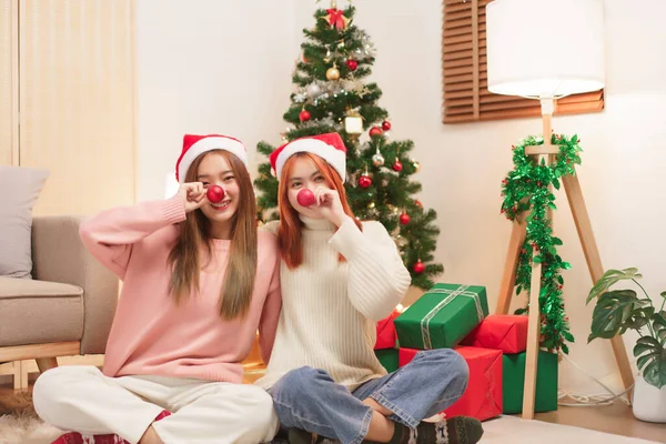 Christmas celebration concept, Two women in santa hat and covering nose with red christmas ball.