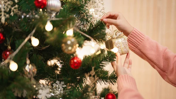 Christmas concept, Young asian woman decorating gold gift on christmas tree in living room at home.