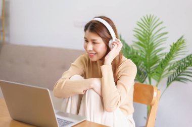 Ev konseptinden çalış, genç Asyalı kadın sandalyede oturup film izlerken kulaklık takıyor..