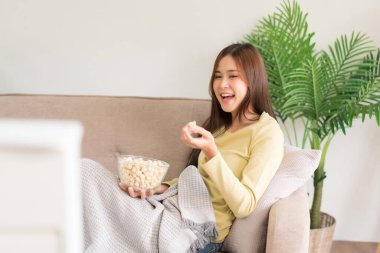 Relaxation concept, Young woman is eating popcorn and laughing while lying on couch to watching tv.