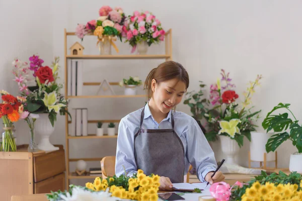 stock image Floristry concept, Woman florist writing orders and customer information in notebook at flower shop.