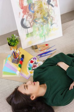 Sanat konsepti, genç Asyalı kadın sanat atölyesinde sanat şaheseriyle yerde yatıyor..