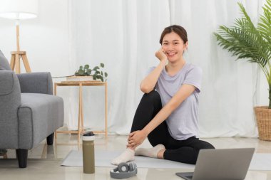 Yoga exercise concept, Young Asian woman sit to relaxing after doing yoga training online at home.