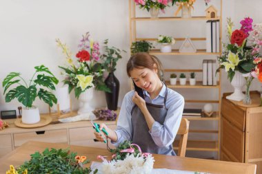 Çiçekçi konsepti, elinde budama makası tutan ve çiçekçide akıllı telefondan konuşan kadın..