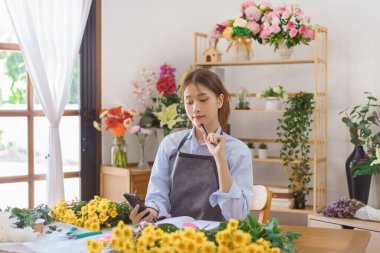 Çiçekçilik konsepti, çiçekçi kadın akıllı telefona bakıyor ve çiçekçide buket tasarlamayı düşünüyor..