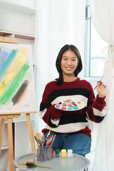 The art concept, Asian female artist holding paint brush and color palette to prepare for painting.