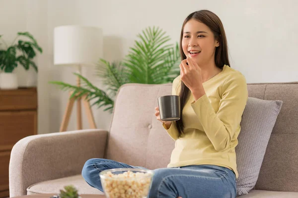 Concept of activity in home, Young woman is drinking coffee and eating popcorn while watching tv.
