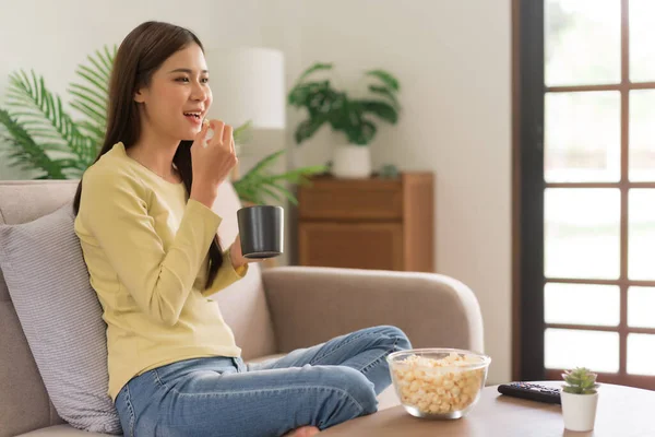 Concept of activity in home, Young woman is drinking coffee and eating popcorn while watching tv.