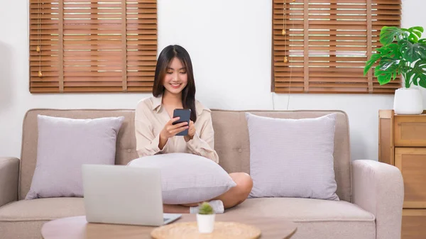 Concept of activity in living room, Asian woman use smartphone to surfing social media on sofa.