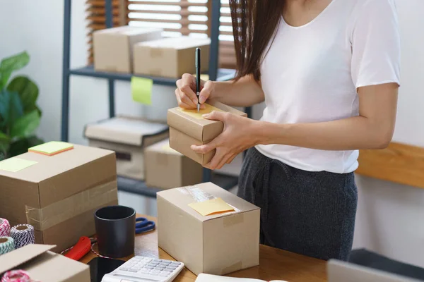 Online selling concept, Asian business women writing address customer on parcel boxes for delivery.