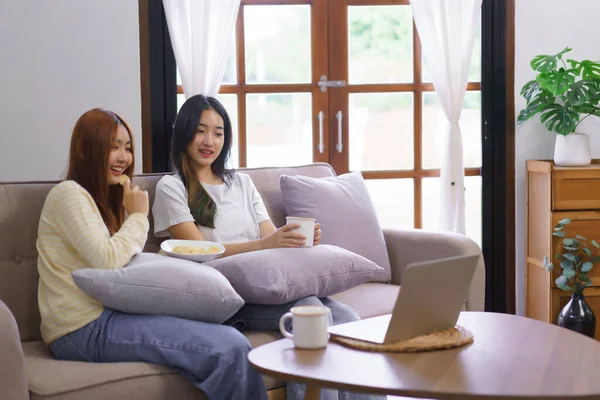 Relax at home concept, Lesbian couple drinks coffee and eating snack while watching movie together.