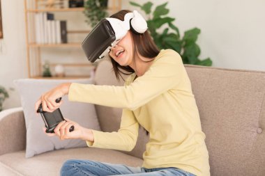 Concept of activity in home, Young woman having fun while playing game with VR glasses and joystick.