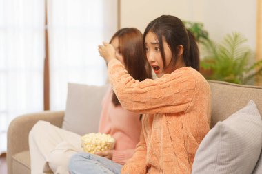 Lifestyle at home concept, LGBT lesbian couple covers eye of girlfriend while watching horror movie.