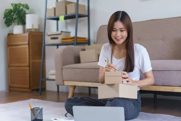 Online selling concept, Asian business women writes address on parcel boxes for delivery to client.