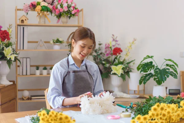 Floristry concept, Woman florist making white chrysanthemum bouquet and tie ribbon at flower shop.