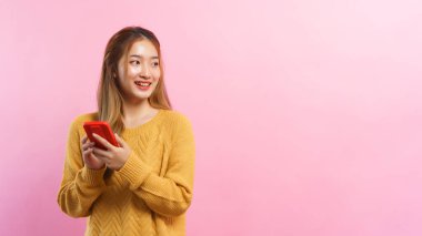 Young women holding smartphone and looking outside with empty space on isolated pink background.