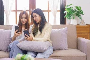 Relax at home concept, LGBT lesbian couple looks on phone and point while shopping online together.
