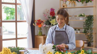 Çiçekçi konsepti, çiçekçi kadın çiçek dükkanında beyaz kasımpatı buketi ve kravat kurdelesi yapıyor..