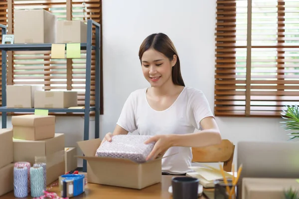 Online selling concept, Asian business women packing product into parcel box for prepare delivery.