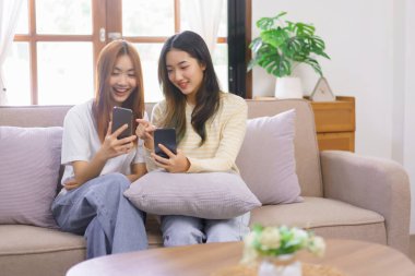 Relax at home concept, LGBT lesbian couple looks on phone and point while shopping online together.
