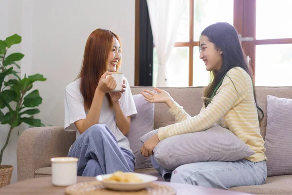 Relax at home concept, LGBT lesbian couple is drinking coffee and talking together in living room.