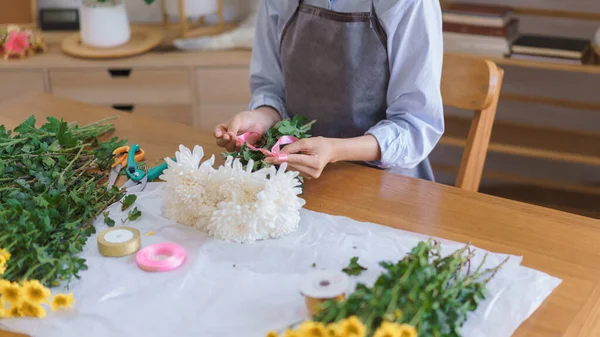 Florist concept, Woman florist making white chrysanthemum bouquet and tie ribbon at flower shop.