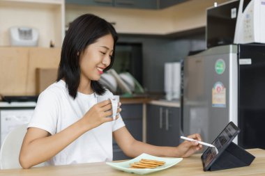 Evde rahatlama konsepti, evde kahve içip kraker yerken tablet kullanan genç bir kadın..
